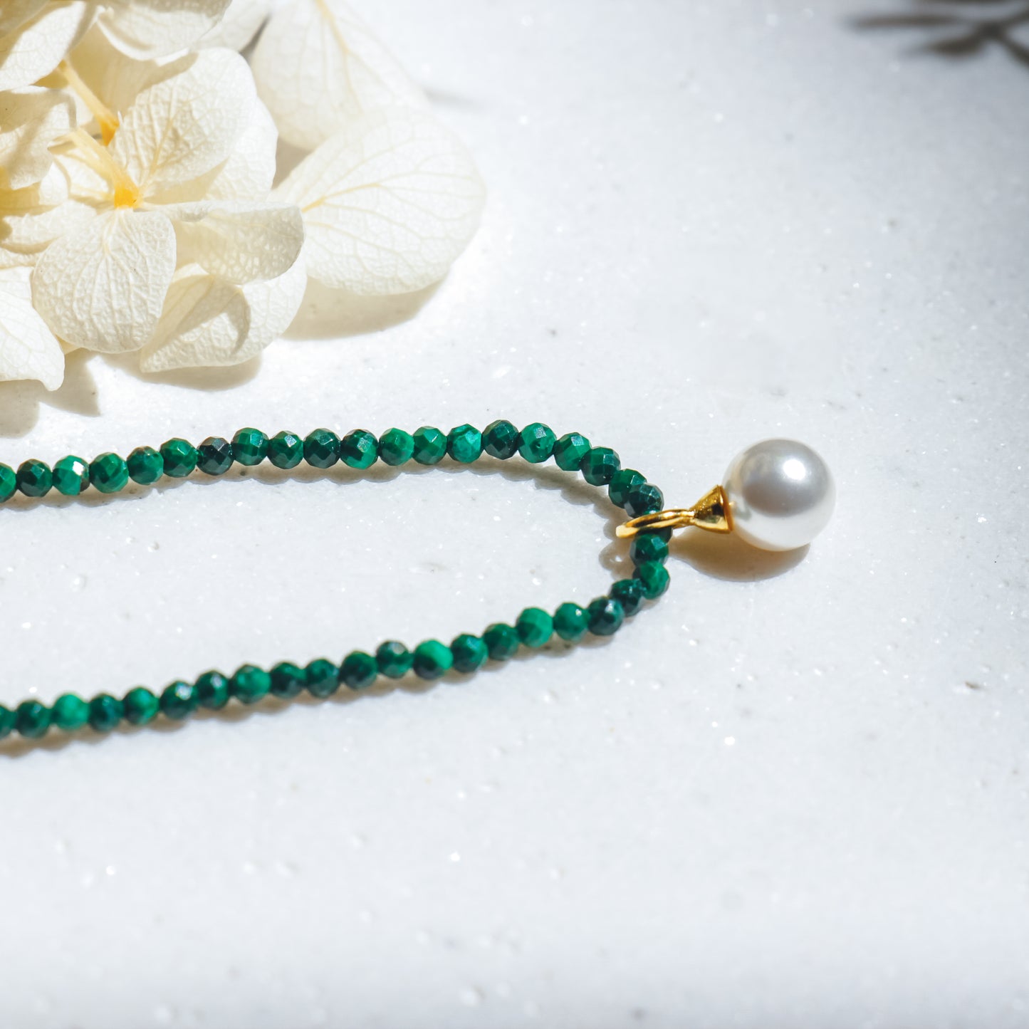 Green beaded necklace with a pearl pendant on a white surface