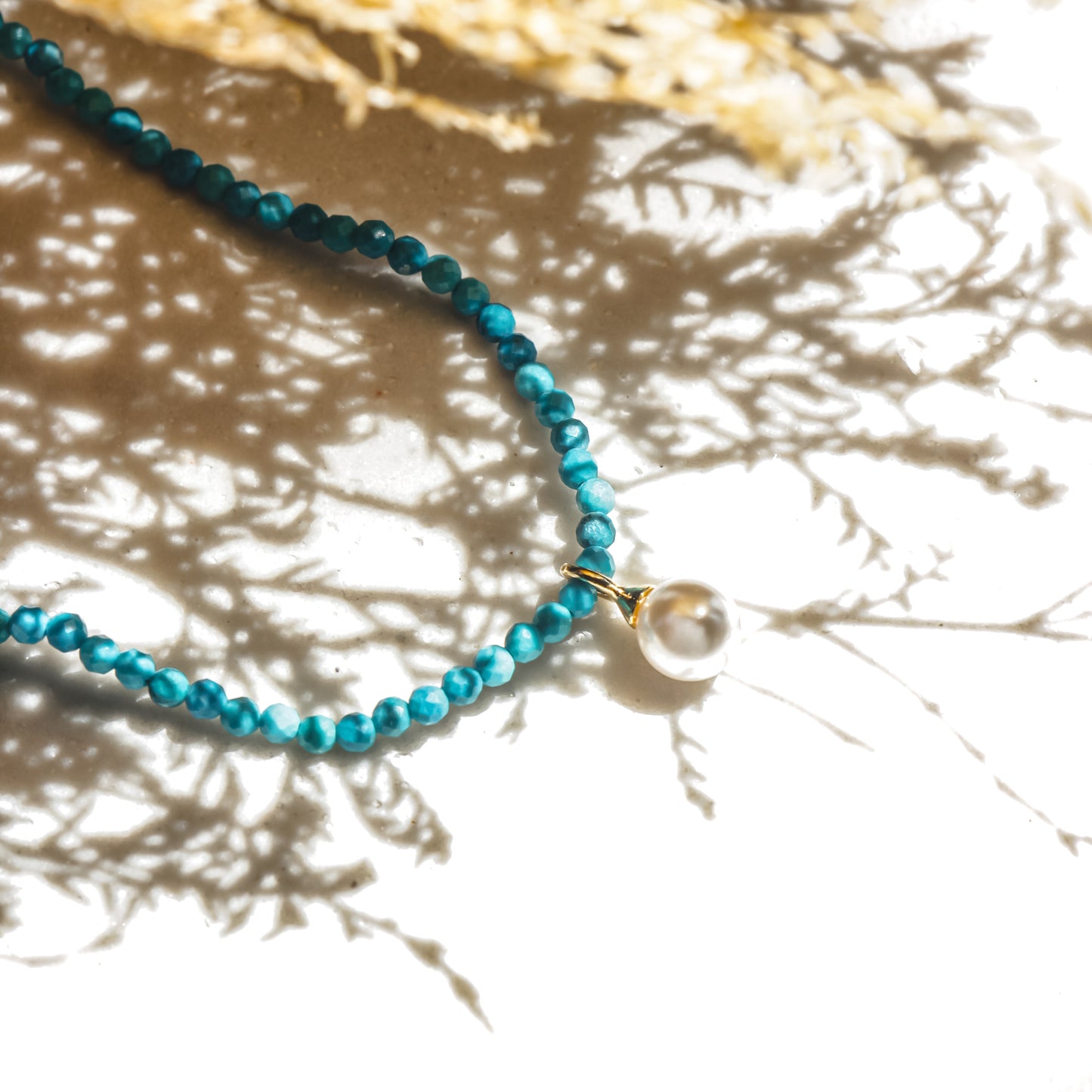 Turquoise beaded necklace with a pearl pendant on a textured surface