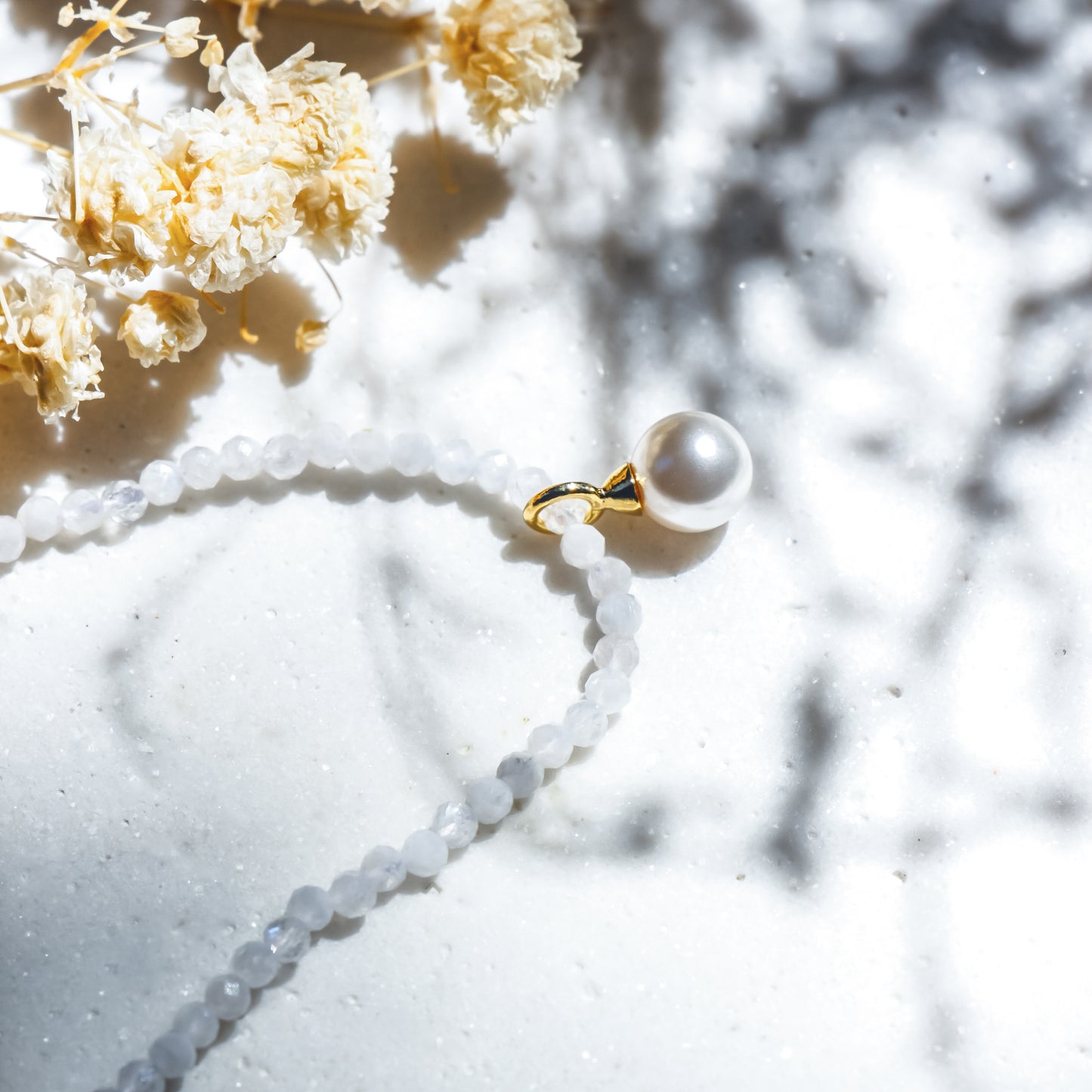 Pearl necklace with a gold clasp on a marble surface with dried flowers.
