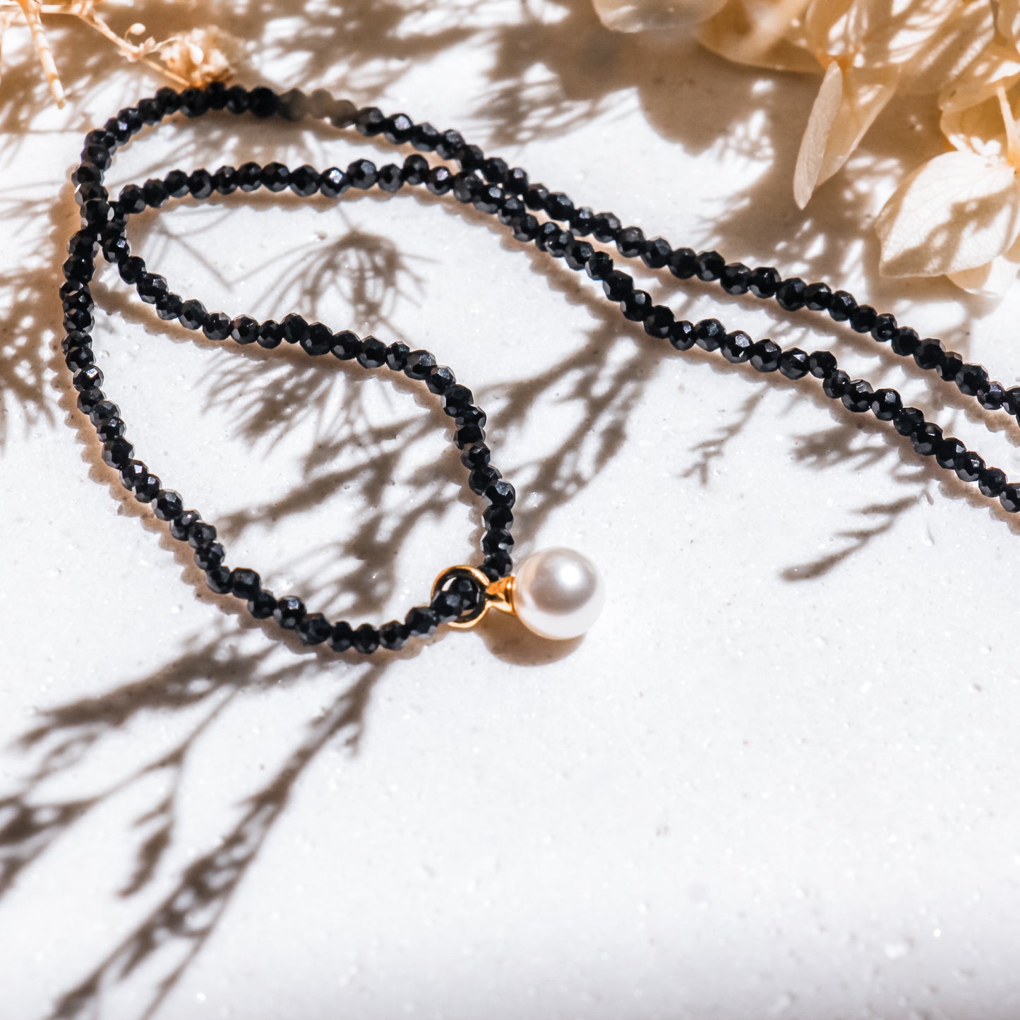 Black beaded necklace with a pearl pendant on a light background