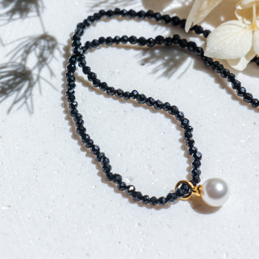 Black beaded necklace with a pearl pendant on a light background