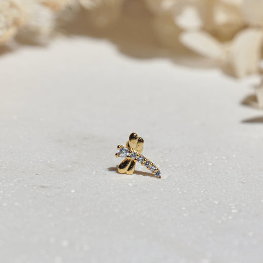 Gold dragonfly earring with gemstones on a white surface with shell background