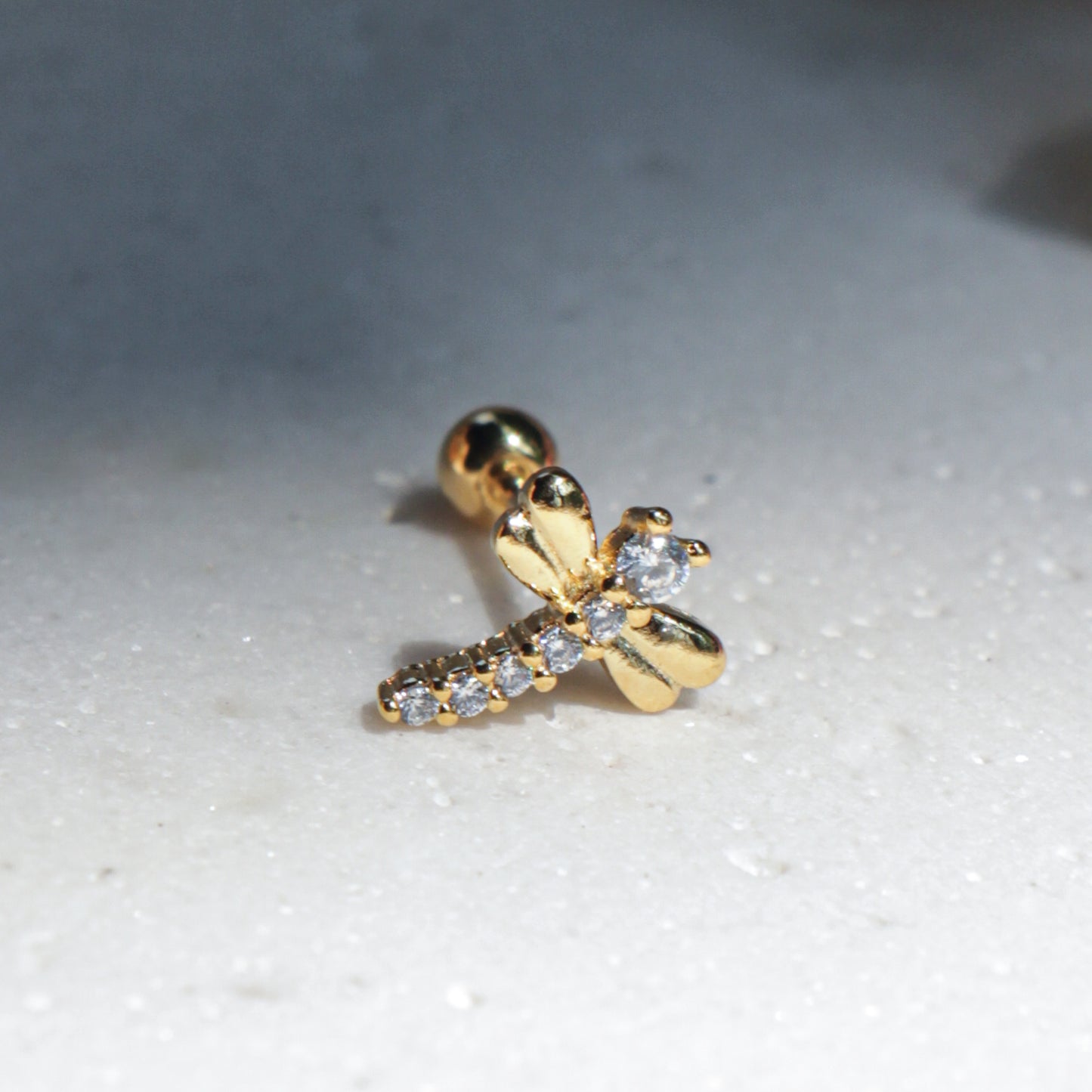 Gold dragonfly earring with a cubic zirconia on a white surface