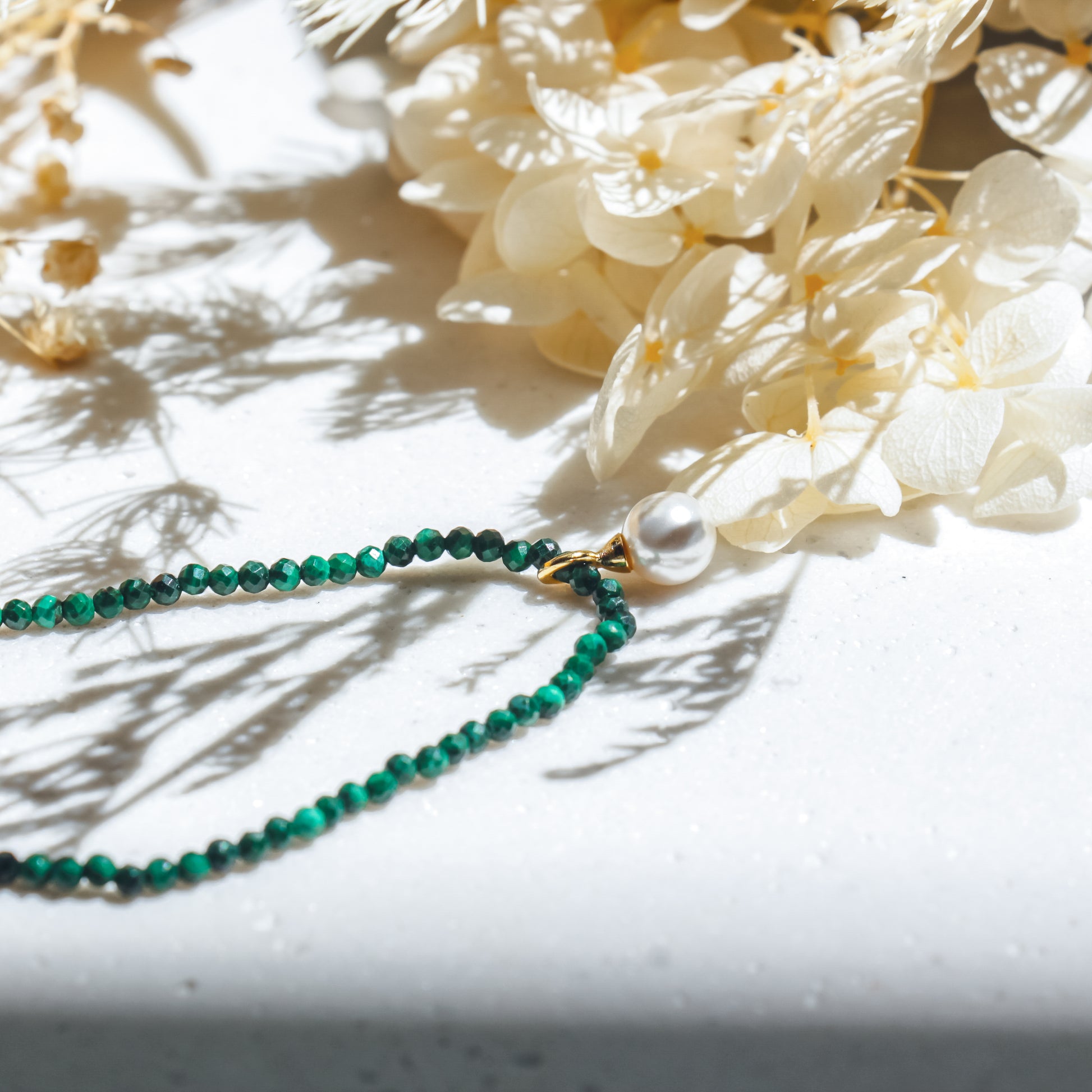 Green beaded necklace on a white surface with white flowers