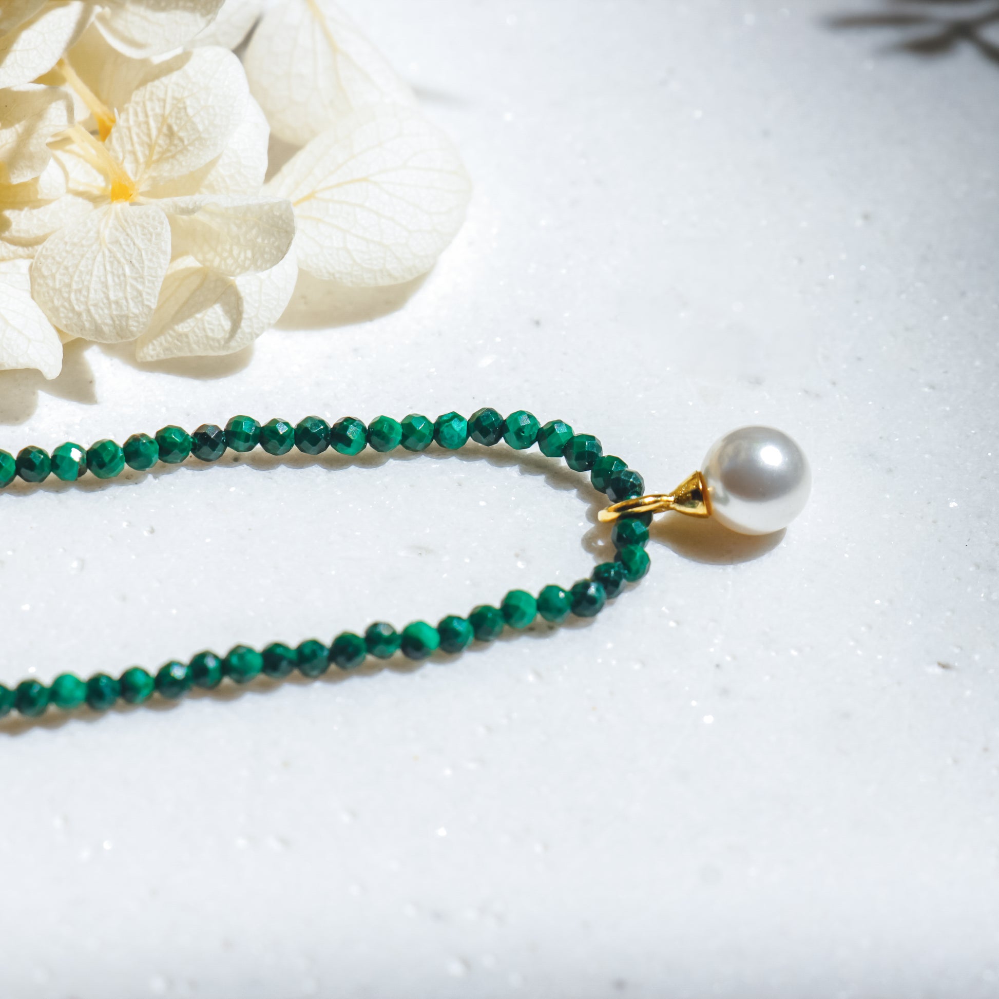 Green beaded necklace with a pearl pendant on a white surface