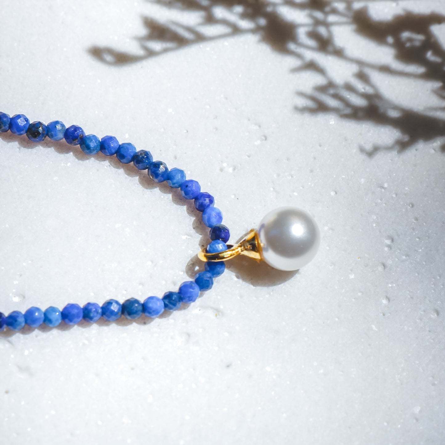 Necklace with blue beads and a pearl pendant on a light background