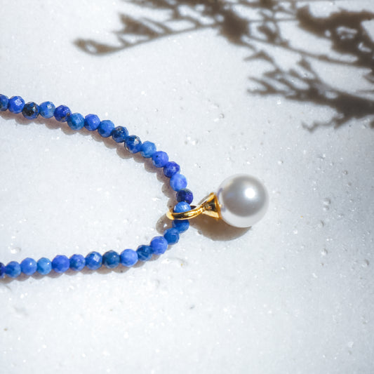 Necklace with blue beads and a pearl pendant on a light background