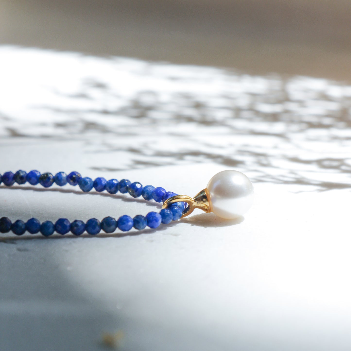 Blue beaded necklace with a pearl pendant on a light background