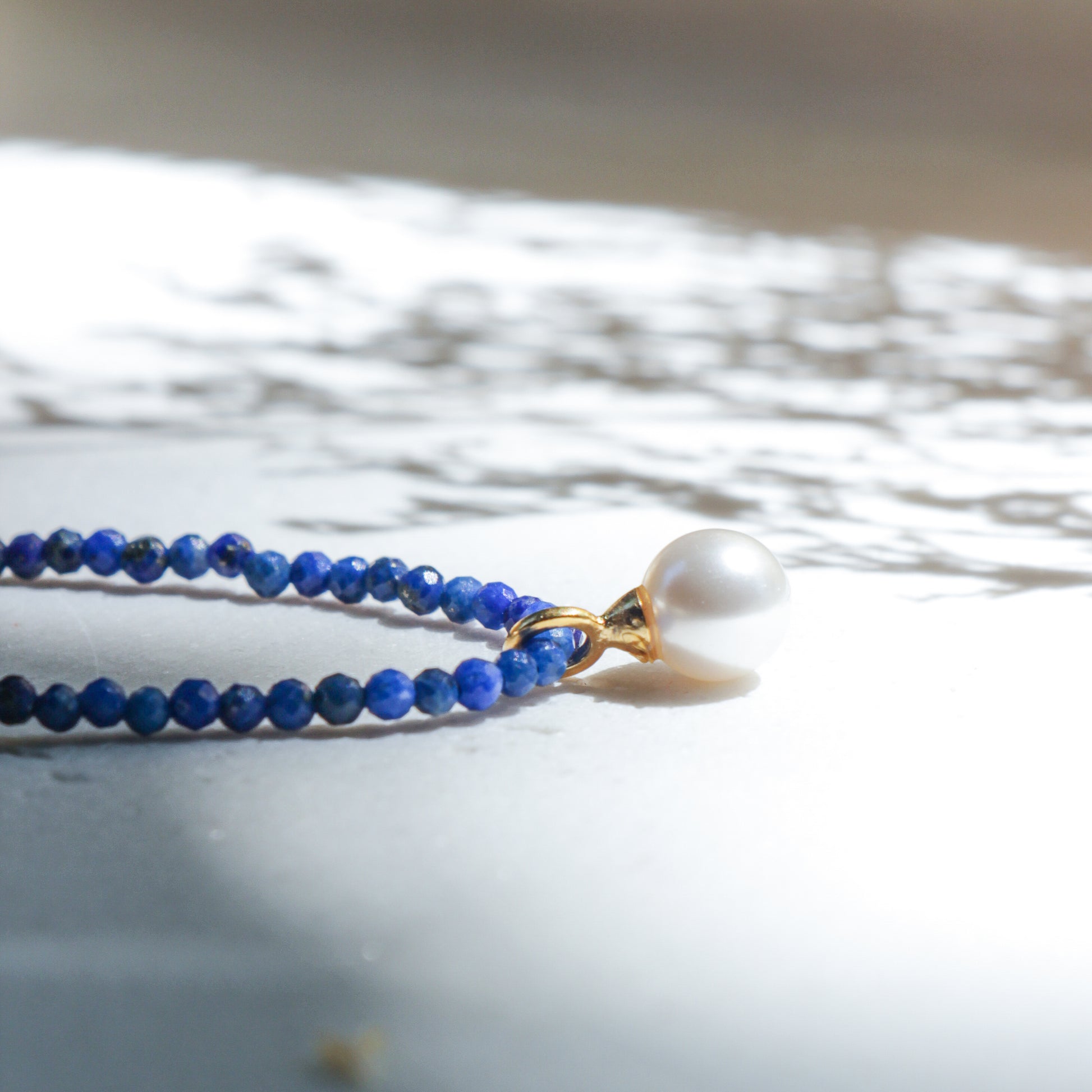 Blue beaded necklace with a pearl pendant on a light background