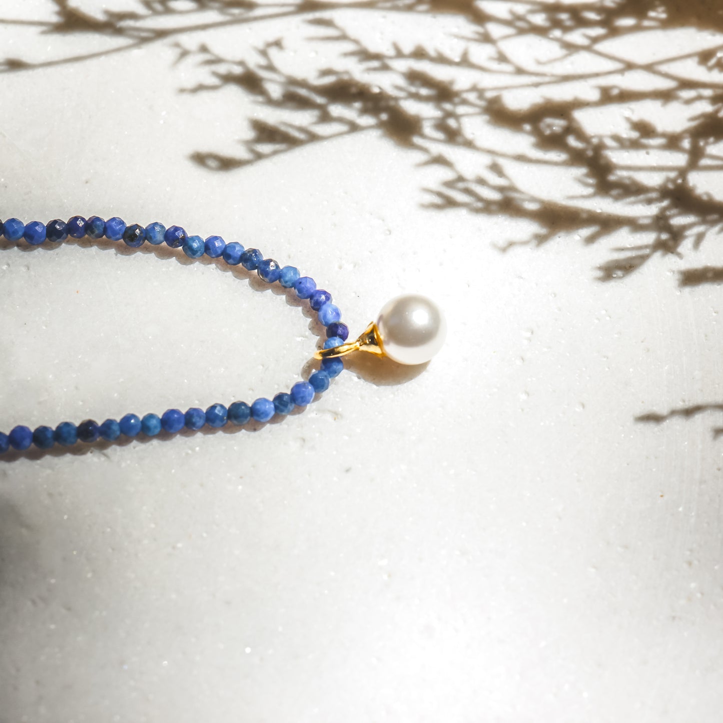 Necklace with blue beads and a pearl pendant on a light surface