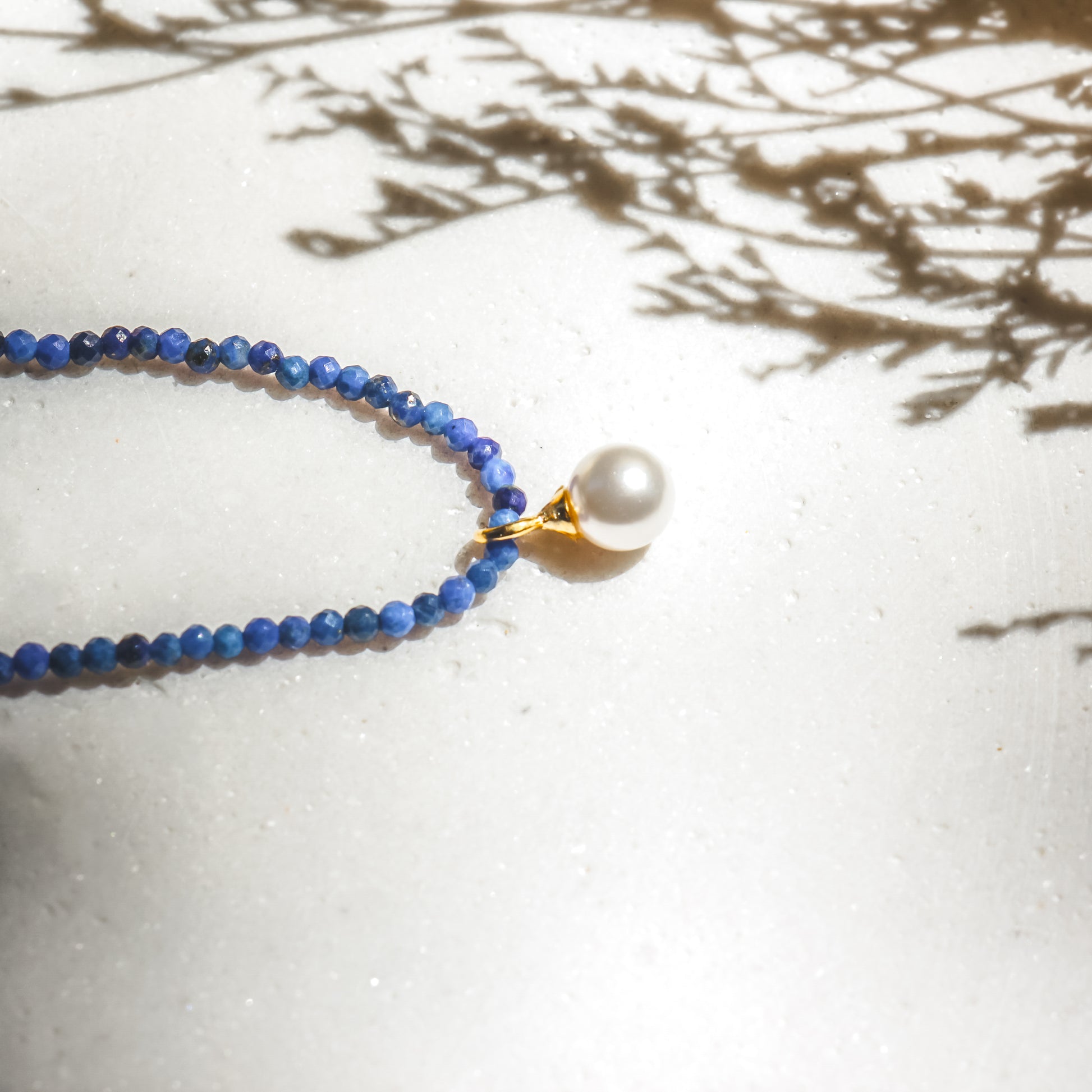 Necklace with blue beads and a pearl pendant on a light surface