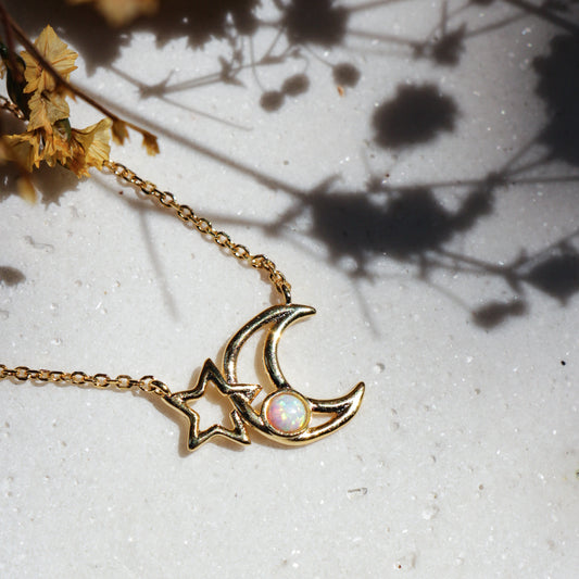 Gold necklace with a moon and star design on a textured surface with shadows.