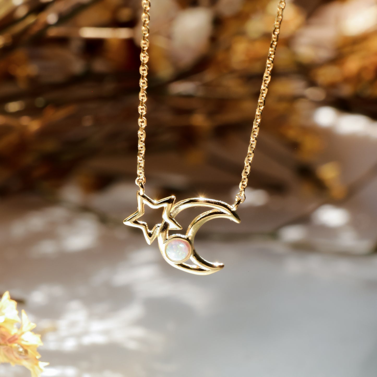 Gold necklace with a star and moon pendant on a blurred natural background