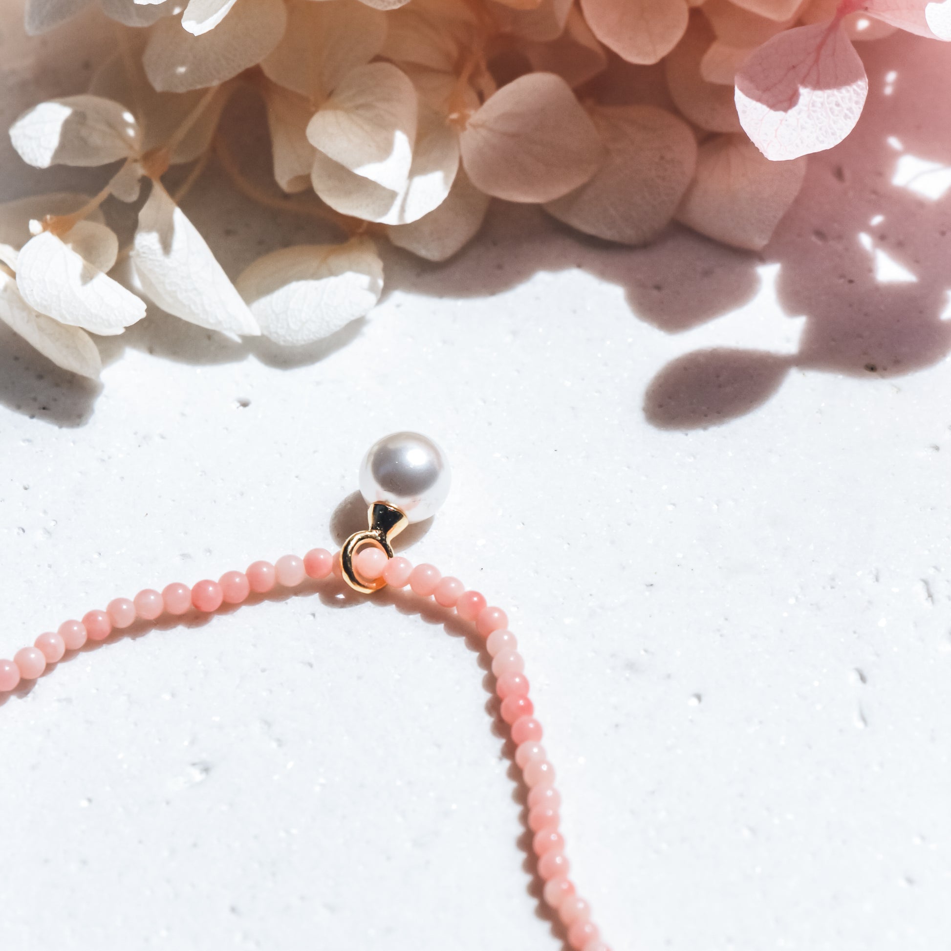 Pearl necklace with coral pink beads on a white surface with flowers in the background