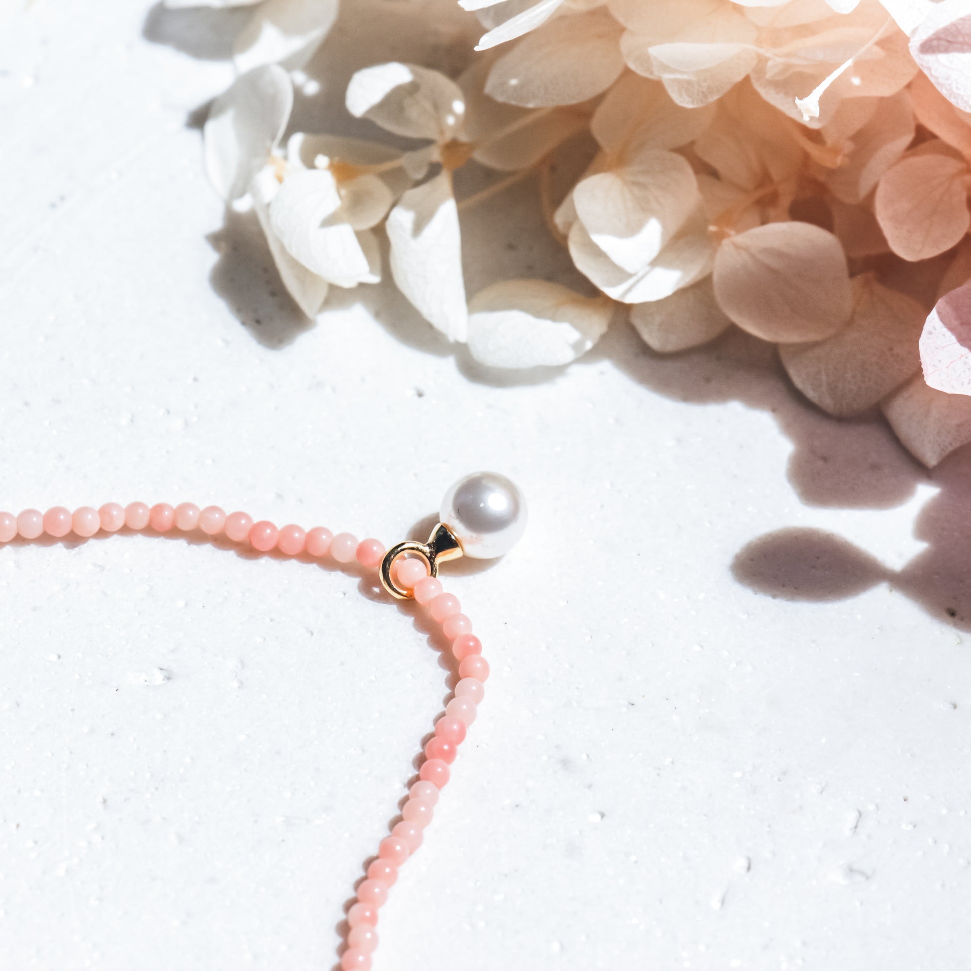 Necklace with pink beads and a pearl pendant on a light background