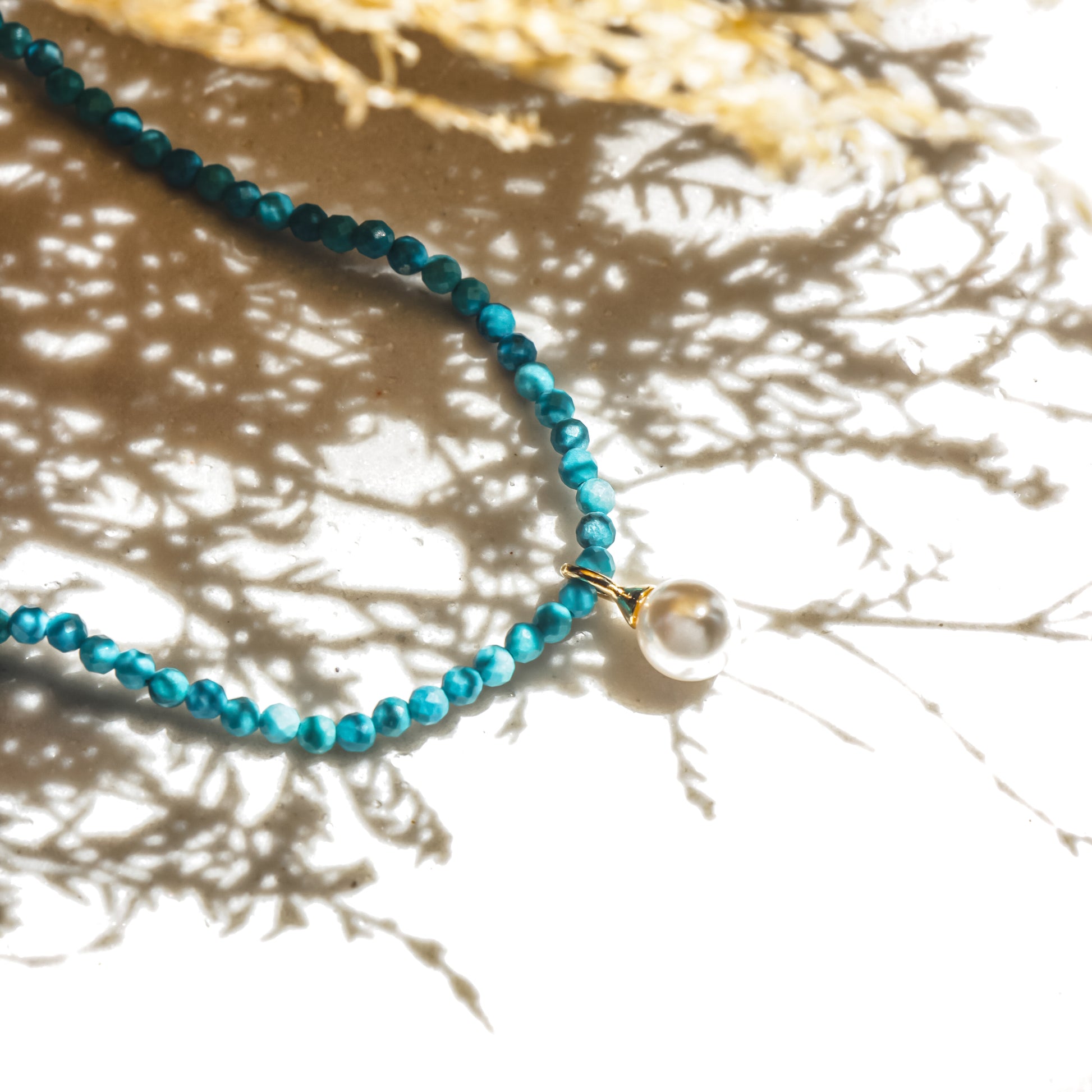 Turquoise beaded necklace with a pearl pendant on a textured surface
