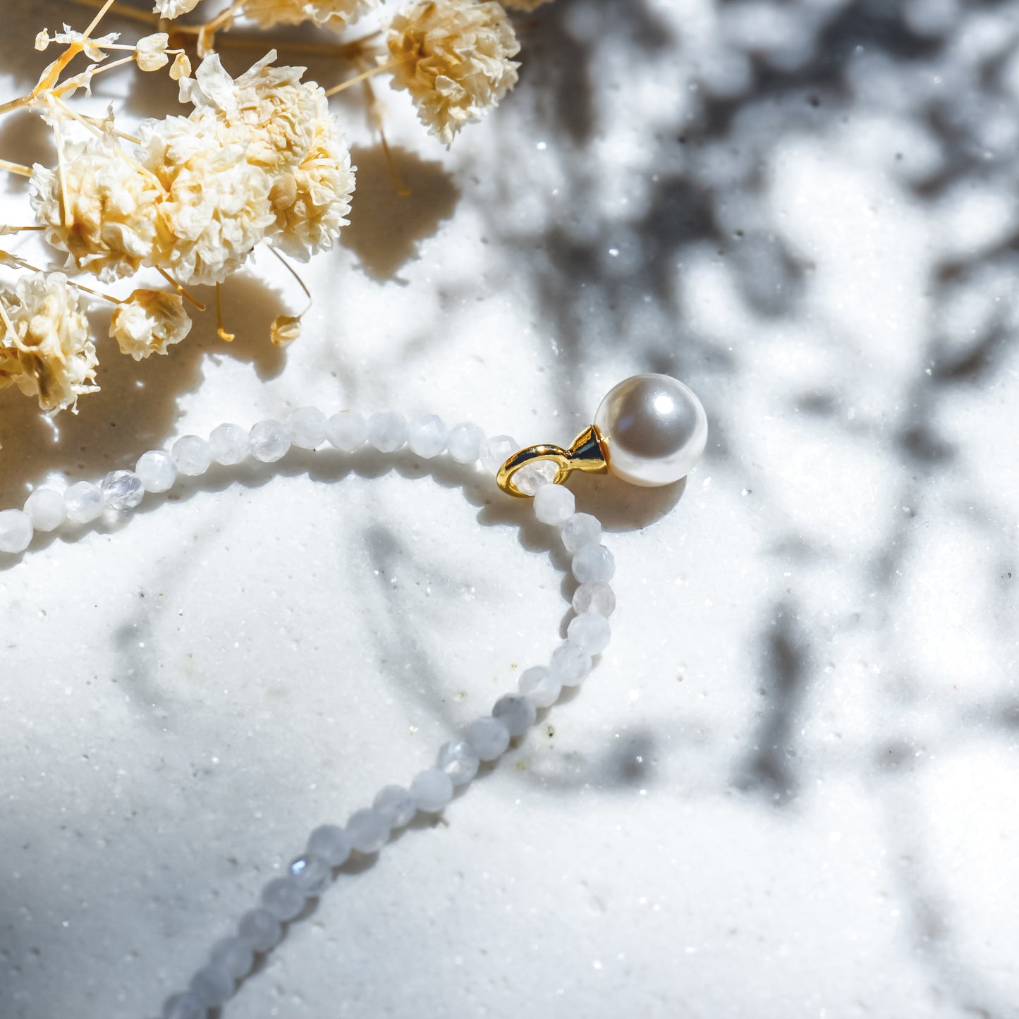 Pearl necklace with gold clasp on a light surface with dried flowers