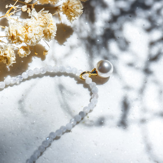 Pearl necklace with gold clasp on a light surface with dried flowers